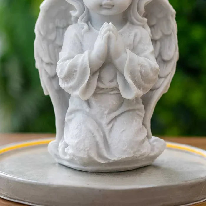 Objeto devocional com figura de anjo orando e iluminação na base