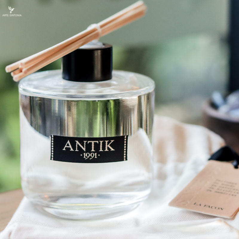 Frasco de vidro arredondado do difusor de ambiente Antik Mangue Vert com varetas de madeira clara ao lado.