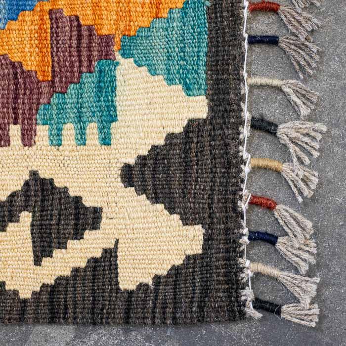Detalhe da trama firme de passadeira artesanal colorida destacando padrões ancestrais e acabamento manual em franjas.