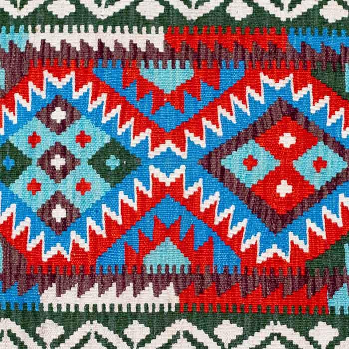 Tapete artesanal Kilim do Afeganistão com grafismos geométricos étnicos coloridos e técnica de tecelagem plana manual.