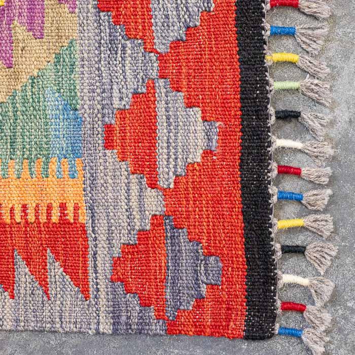 Detalhe da superfície firme de passadeira colorida destacando losangos étnicos e acabamento manual em franjas.