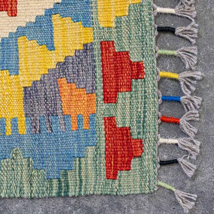 Detalhe da trama firme de tapete artesanal colorido destacando padrões ancestrais e acabamento manual em franjas.