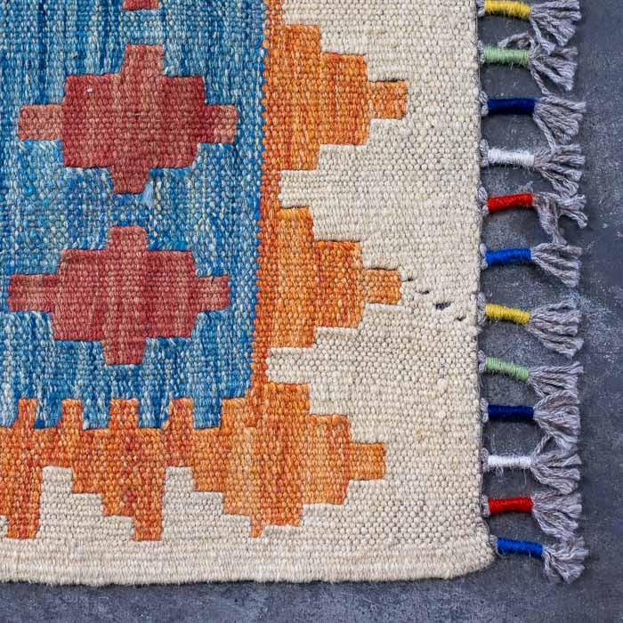 Carpete artesanal afegão de tecelagem plana com franjas coloridas nas extremidades.