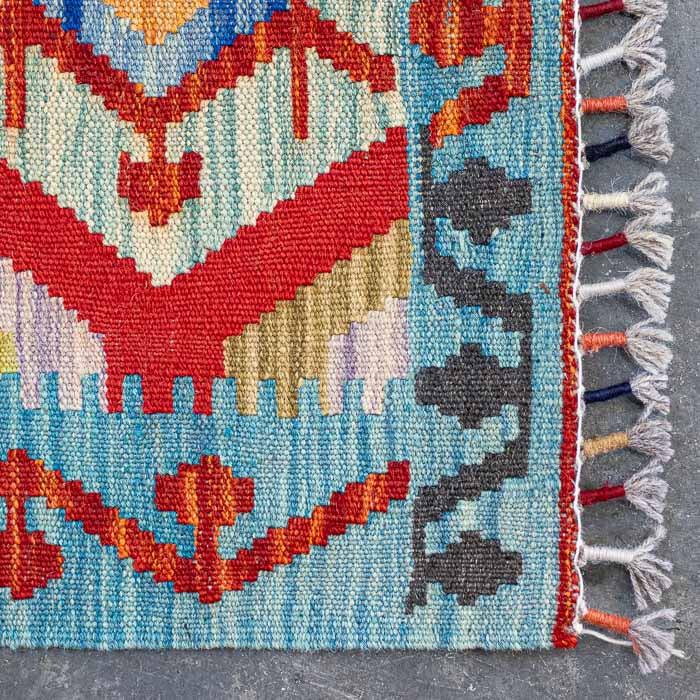 Detalhe da trama firme e colorida de passadeira Kilim artesanal destacando losangos étnicos e acabamento em franjas.
