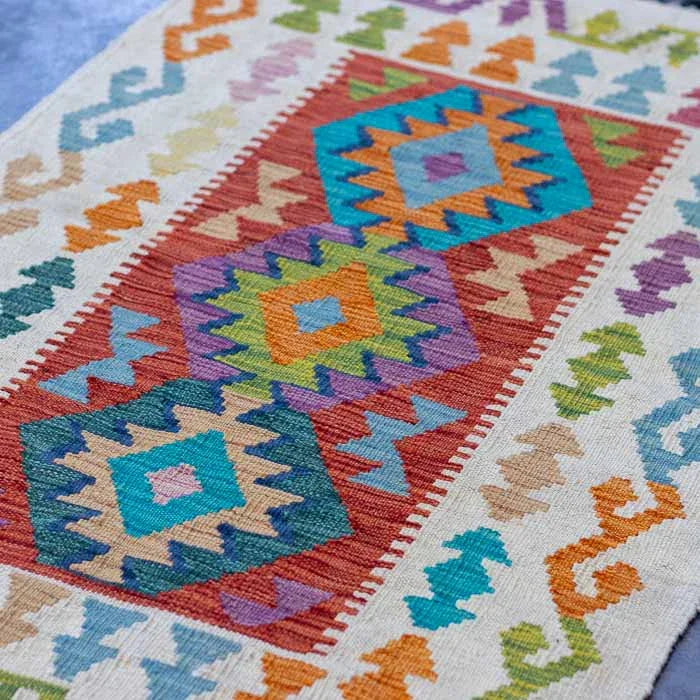 Kilim afegão de 125cm com design orgânico sobre superfície de cimento queimado.