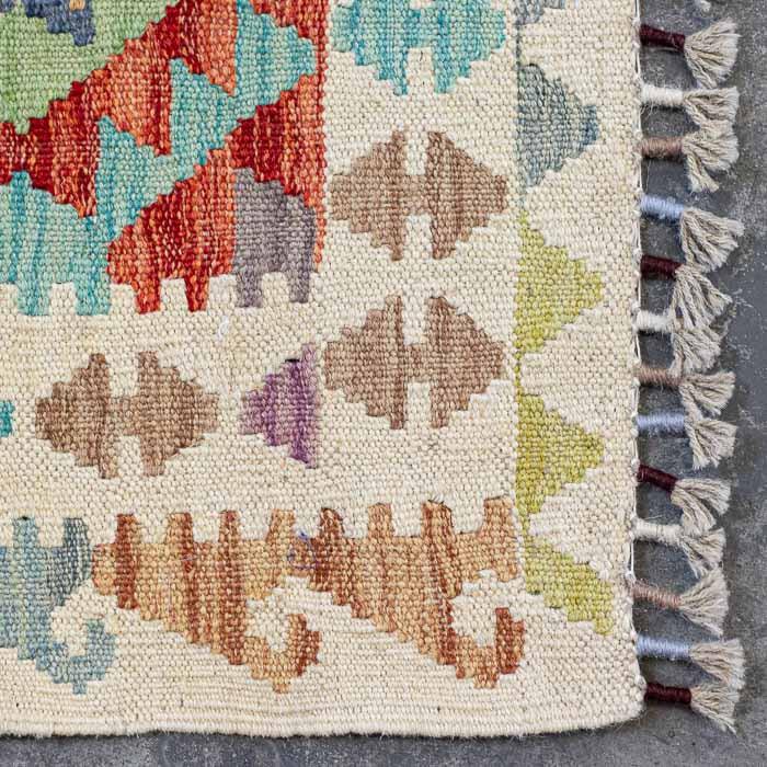 Detalhe da trama firme e colorida de passadeira Kilim artesanal destacando losangos étnicos e acabamento em franjas.