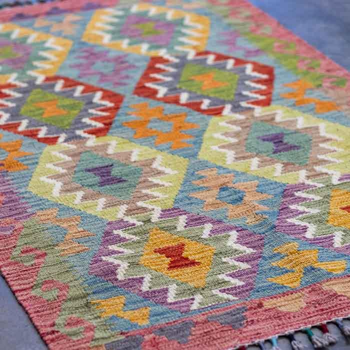 Kilim afegão de 125cm com design orgânico sobre superfície de cimento queimado.