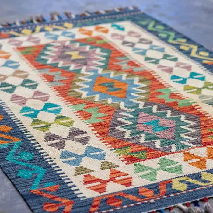 Kilim afegão de 125cm com cores vibrantes e design orgânico sobre piso escuro.