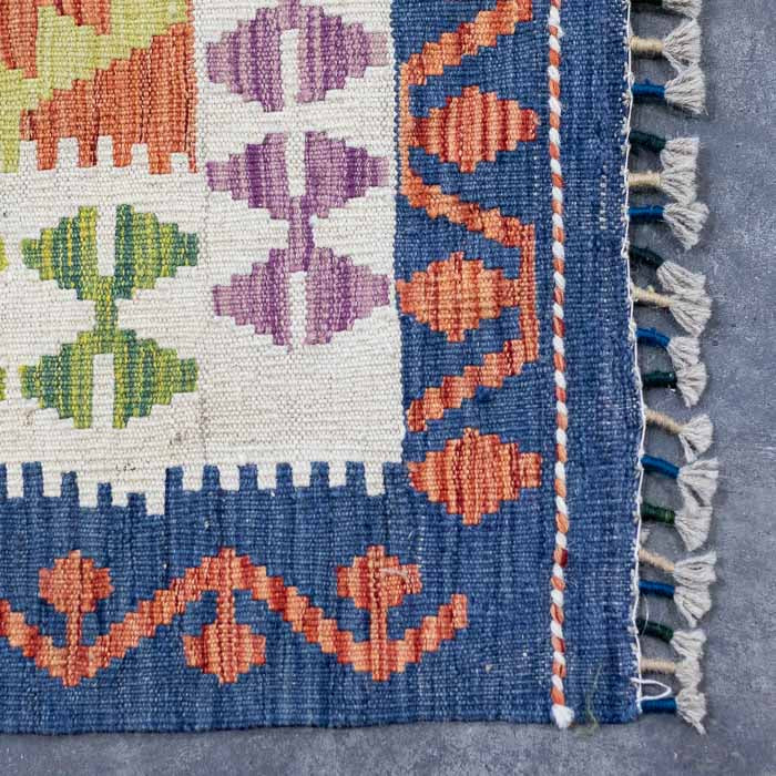Detalhe da tecelagem manual firme de tapete colorido destacando padrões ancestrais em lã e acabamento artesanal em franjas.