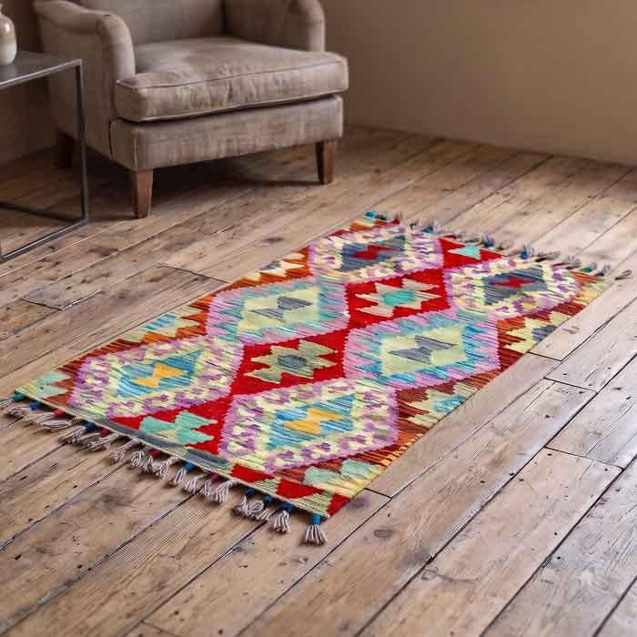 Tapete pequeno estilo étnico com desenhos de losangos e franjas coloridas.