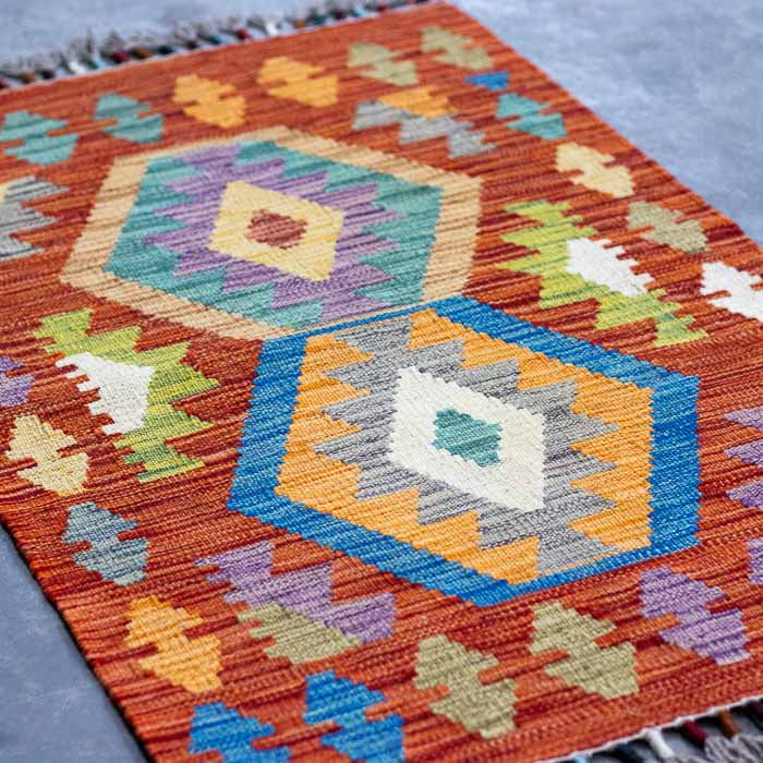 Kilim afegão de 97cm com design orgânico sobre superfície de cimento queimado.