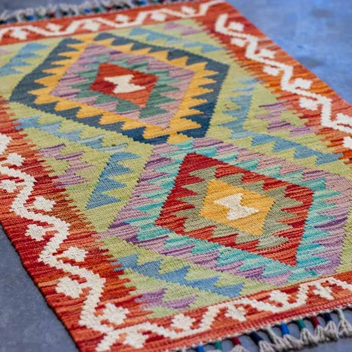 Detalhe da trama firme de tapete artesanal colorido destacando padrões ancestrais e acabamento manual em franjas.