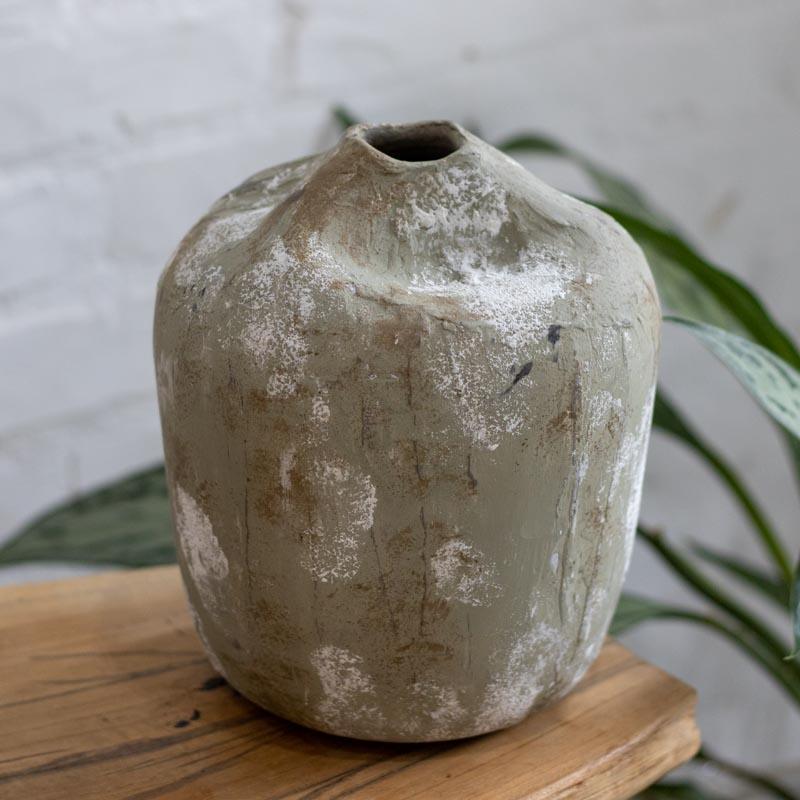 Peça de cerâmica brasileira de 20cm de altura com design orgânico contra fundo de tijolos brancos.