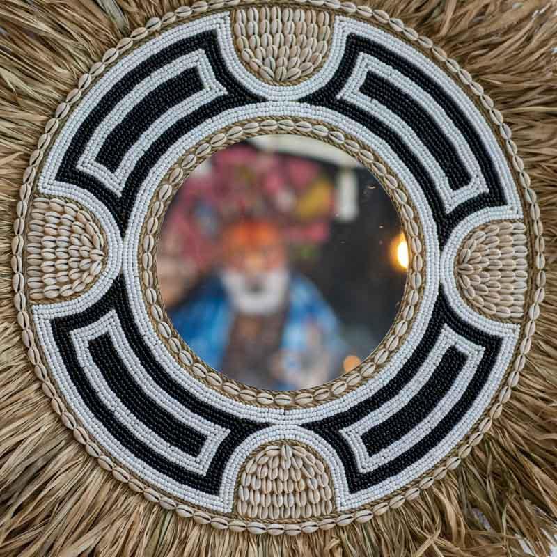 Espelho redondo Dewa artesanal de Bali com moldura em fibra natural, miçangas pretas e brancas e aplicações de búzios.