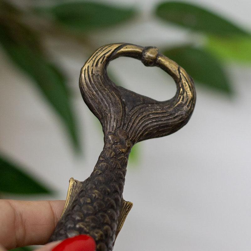 Detalhe do abridor artesanal em bronze dourado em formato de sereia.