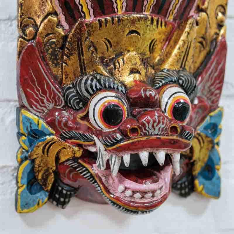 Máscara espiritual de Bali em madeira colorida instalada em parede de tons neutros para decoração étnica.
