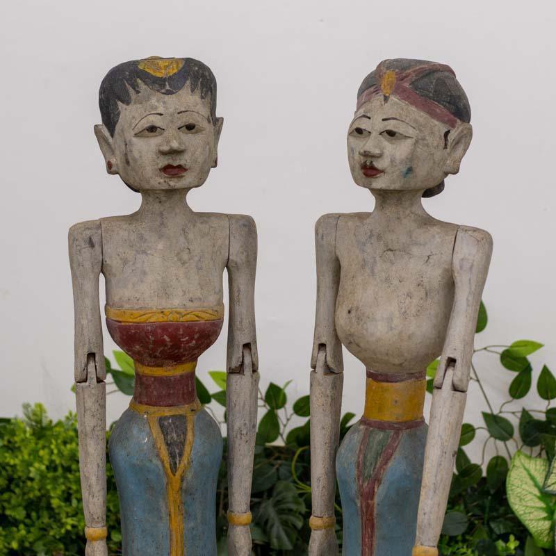 Casal de bonecos de madeira balineses com braços que se movem, uma peça de arte interativa que celebra a tradição de Java e Bali.