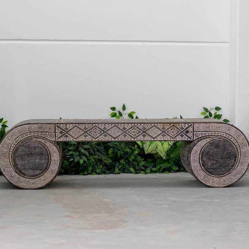 Banco baixo artesanal em madeira maciça da Ilha de Timor, apresentando entalhes tribais detalhados e acabamento rústico escuro.