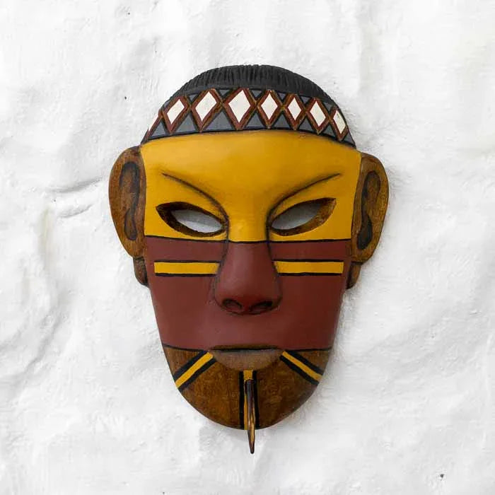 Máscara indígena artesanal entalhada em madeira com pintura tradicional Pataxó em amarelo e vermelho.