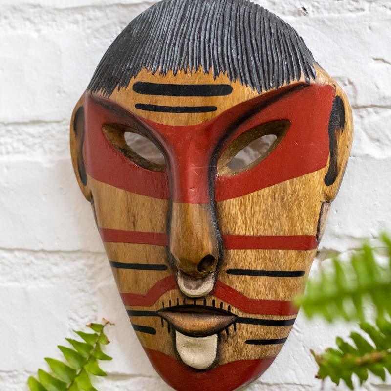 Máscara tribal artesanal esculpida em madeira pelo povo Matsés, com pinturas horizontais vermelhas e detalhe de tiara esculpida no topo.