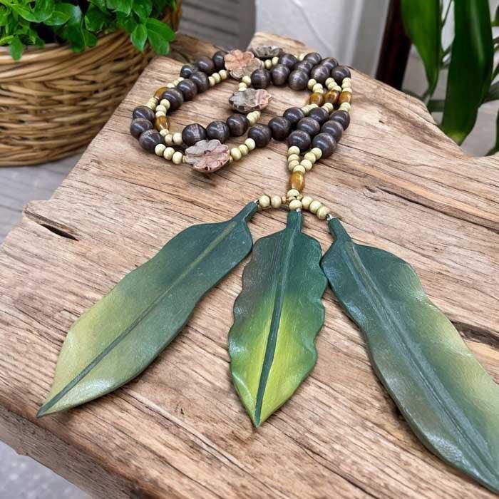 Colar de mesa artesanal brasileiro feito com contas de madeira escura e pingentes de penas esculpidas em tons de verde.