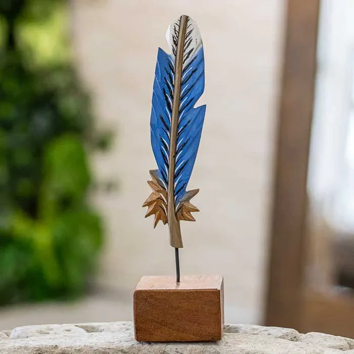 Escultura artesanal em madeira representando uma pena, feita no Brasil.