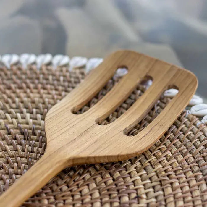 Espátula vazada artesanal em madeira teca produzida em Bali com acabamento fosco polido e cabo anatômico ideal para cozinhar e servir alimentos.