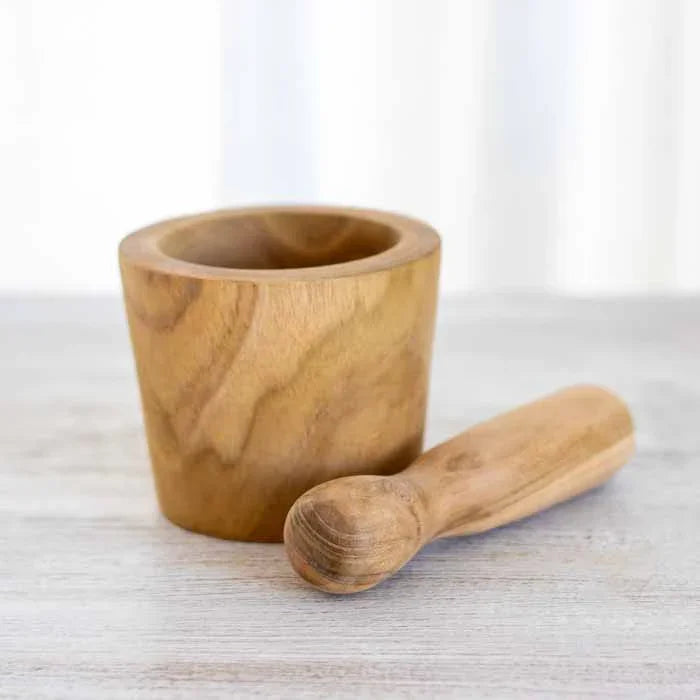 Almofariz artesanal em madeira teca com pistilo coordenado sobre fundo claro.