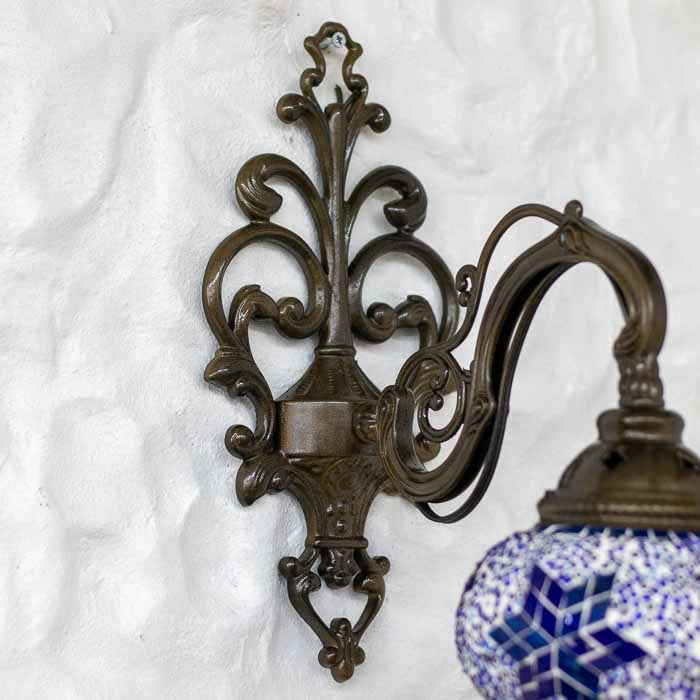 Arandela de metal bronzeado com arabescos clássicos e globo de vidro colorido instalada em parede branca.