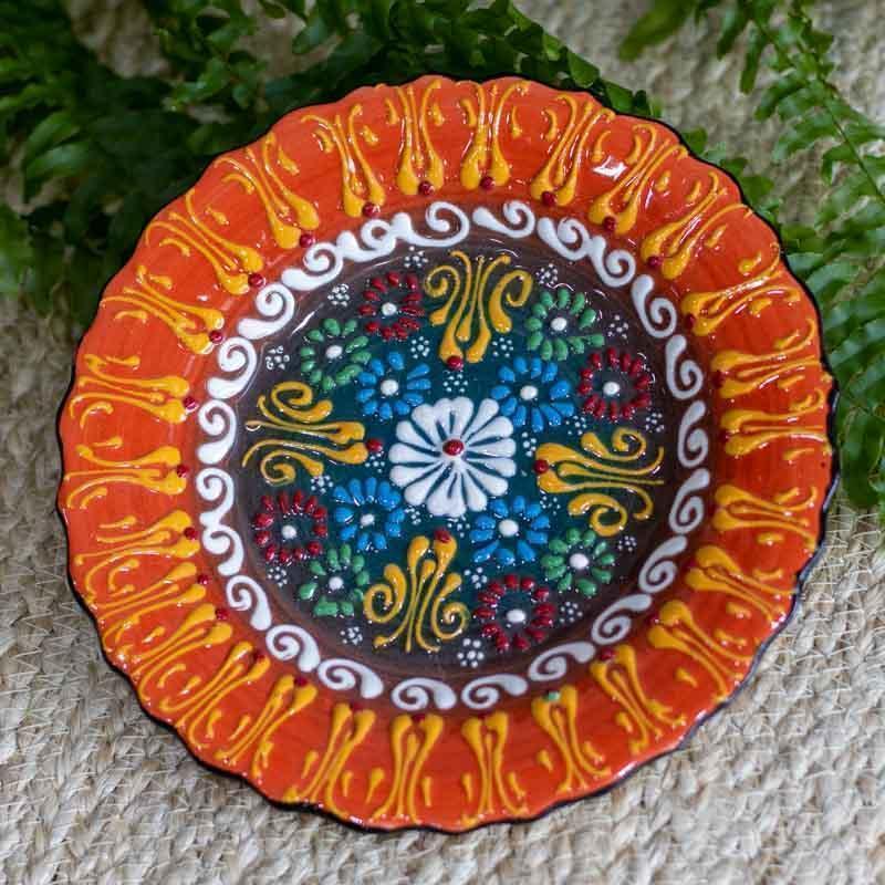 Detalhe da textura em relevo e brilho vítreo de prato cerâmico colorido com desenhos geométricos e florais orientais.