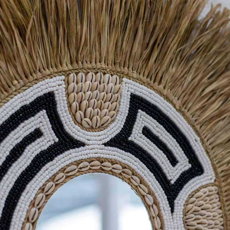 Espelho redondo artesanal de Ubud, Bali, com moldura em fibra natural franjada, búzios e miçangas brancas e pretas.