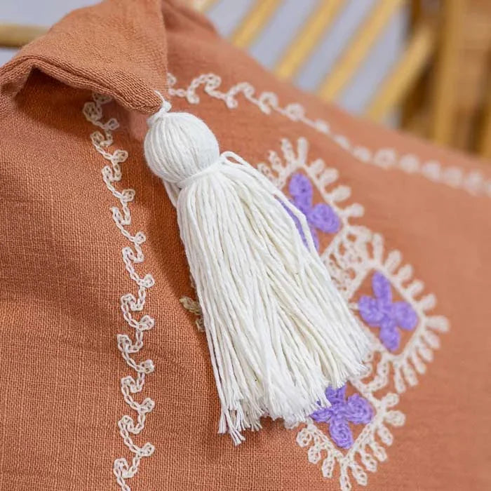 Bordado geométrico em lilás e marrom no centro da almofada decorativa.