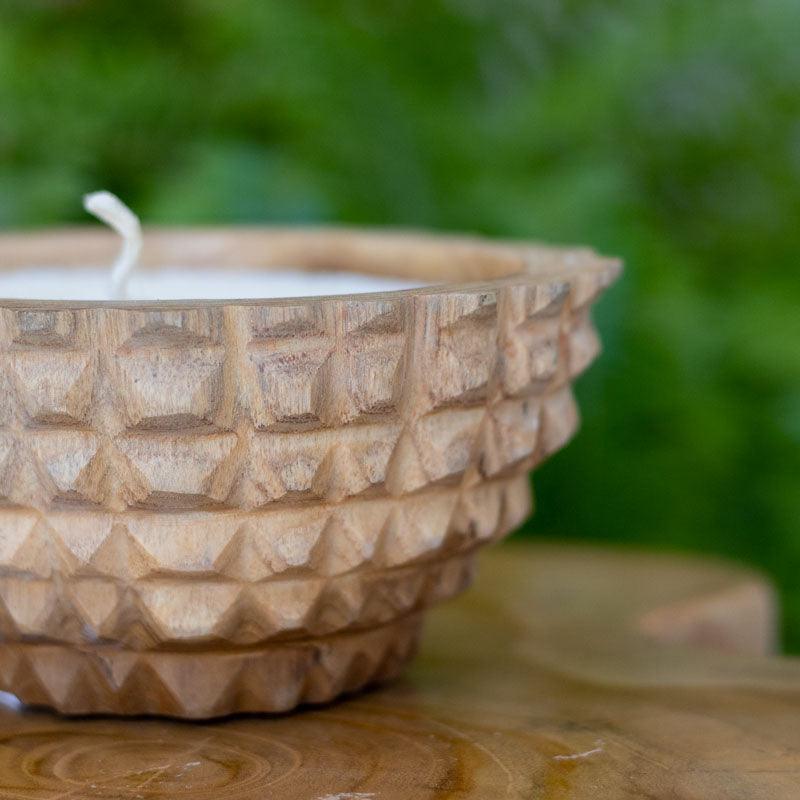 Objeto decorativo balinês com vela branca em recipiente orgânico de madeira sobre mesa de centro moderna.