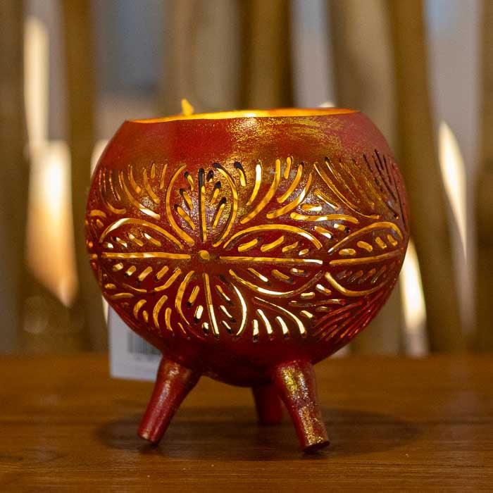 Porta-vela em coco com recortes manuais que criam sombras decorativas no ambiente.
