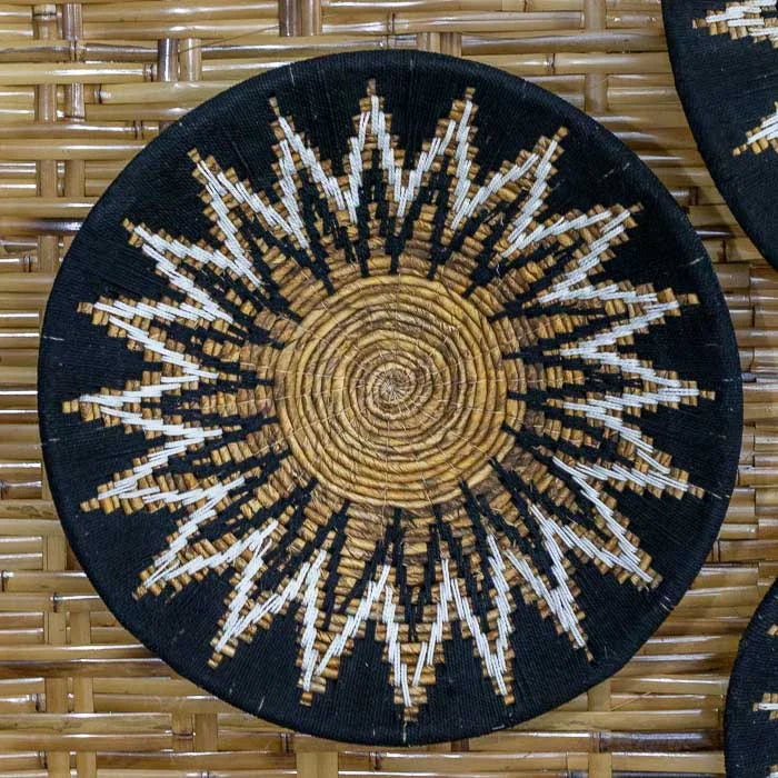 Cestaria artesanal de parede em formato de sol, trançada à mão com fibras naturais escuras em Bali.