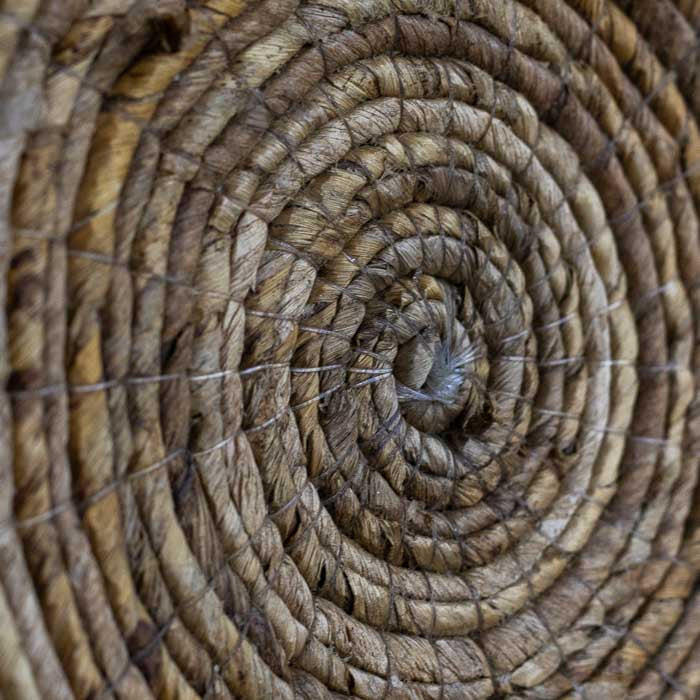 Cestaria artesanal de parede em formato de sol, trançada à mão com fibras naturais escuras em Bali.