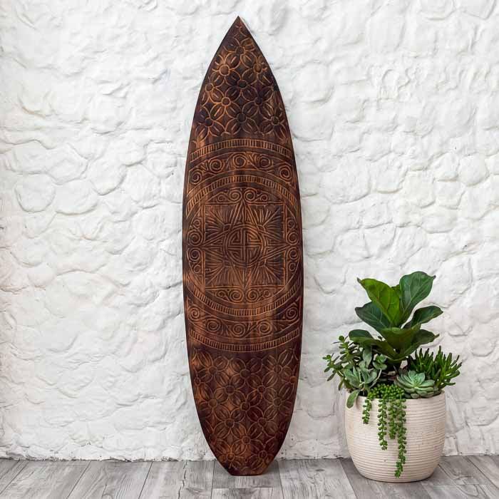 Prancha étnica em madeira entalhada manualmente por artesãos de Timor, com desenhos tribais em espiral e formas geométricas que simbolizam harmonia e ancestralidade.
