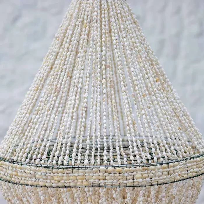 Luminária decorativa pendente estilo boho chic inteiramente revestida com búzios e conchas marinhas claras.