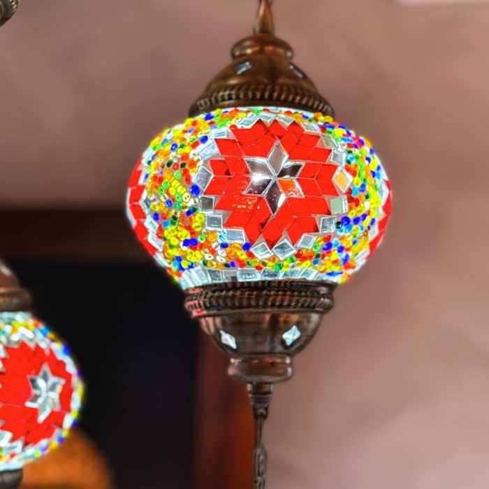 Lustre oriental de teto com mosaicos vibrantes projetando padrões de luz colorida nas paredes de uma sala de estar.