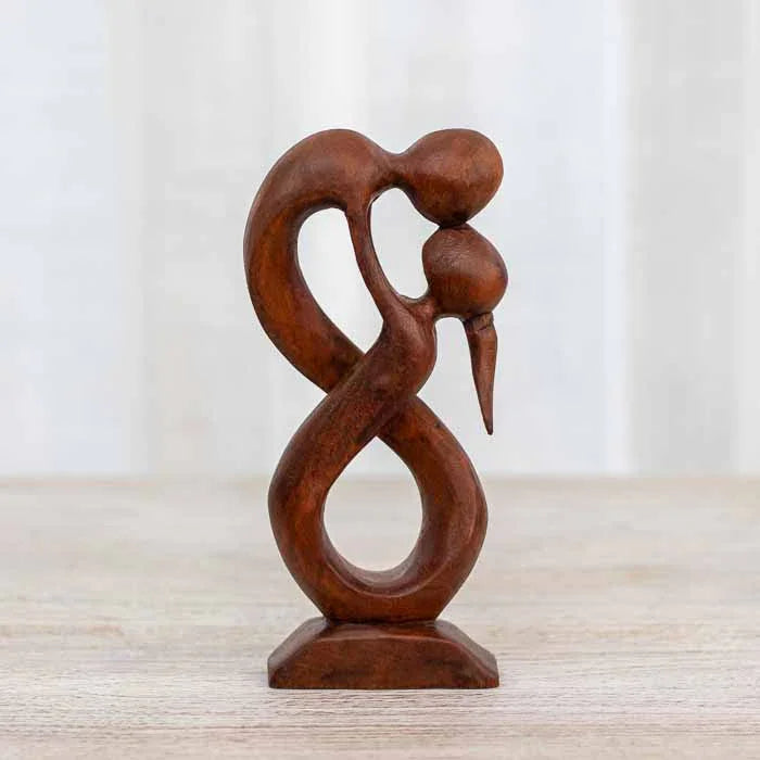 Escultura Amor Infinito em madeira sobre superfície rústica com fundo neutro.