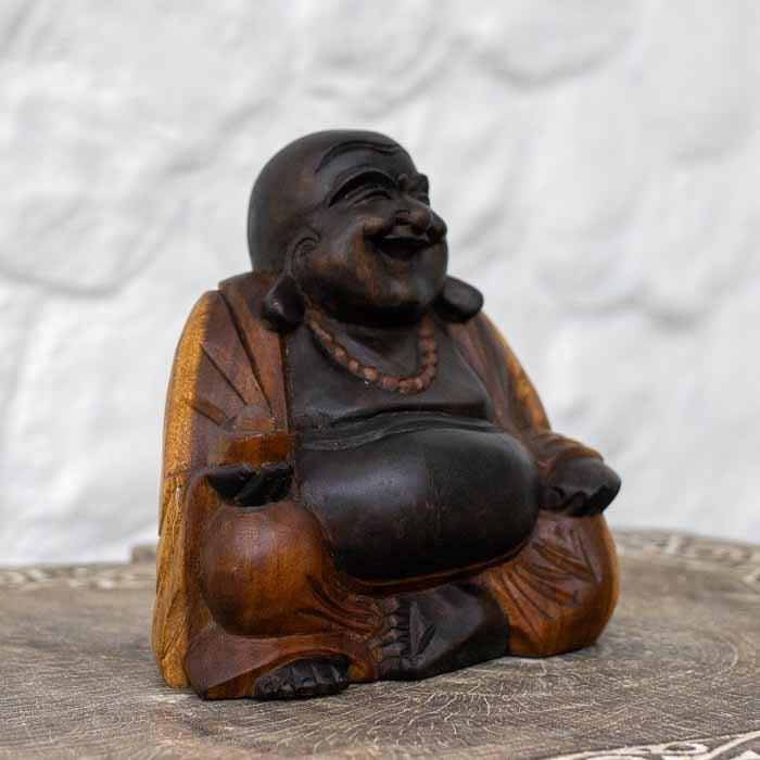 Buda de 20cm em madeira maciça posicionado sobre base rústica em ambiente iluminado.