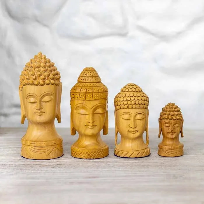 Quatro esculturas da cabeça de Buda em madeira clara entalhada alinhadas por tamanho.