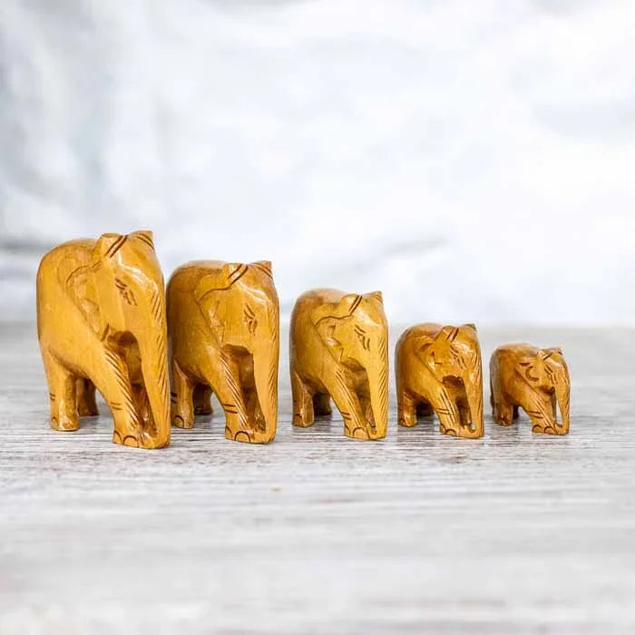 Cinco mini esculturas de elefante em madeira clara entalhada alinhadas por tamanho.