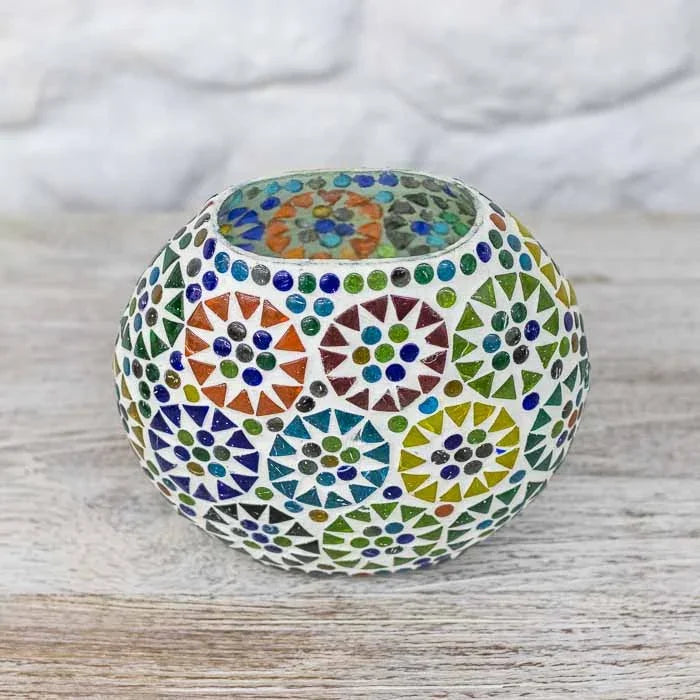 Luminária de mesa esférica em mosaico de vidro colorido acesa sobre superfície rústica.
