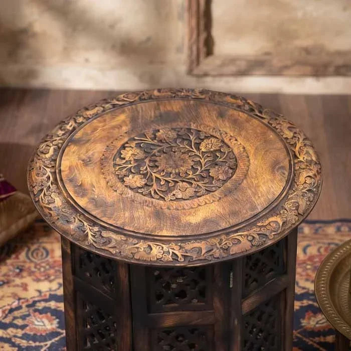 Detalhe dos entalhes florais minuciosos no tampo circular da mesa de apoio.