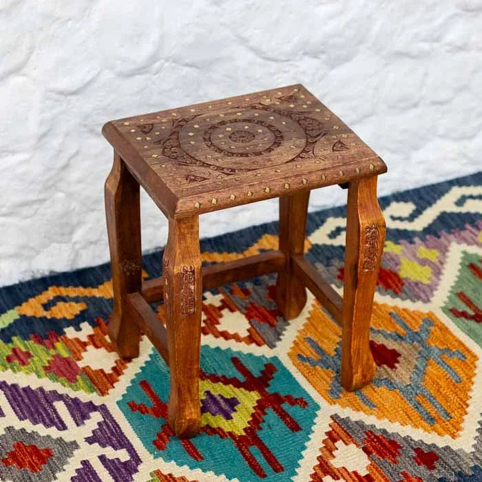 Mesinha de canto decorativa de estilo oriental com pés trabalhados sobre tapete étnico.