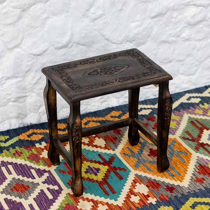 Mesinha de canto decorativa de estilo oriental com acabamento escuro e pés curvados sobre tapete ético.