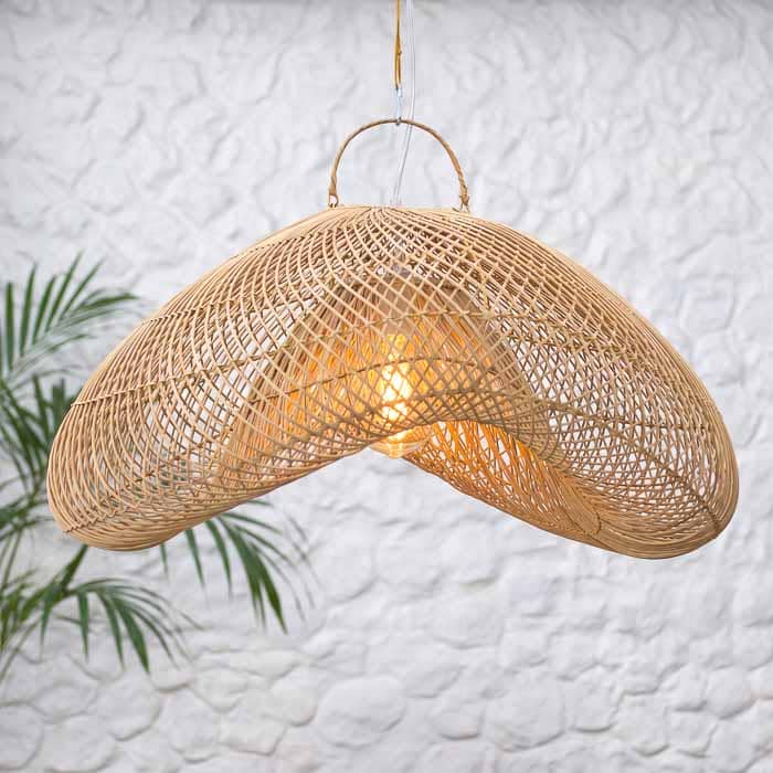 Lustre de rattan em formato fluído posicionado em sala com teto de madeira e decoração rústica.