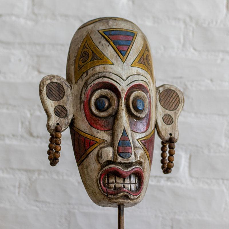 Detalhe da fisionomia expressiva e dos grafismos étnicos em máscara de guerreiro artesanal importada da Indonésia.