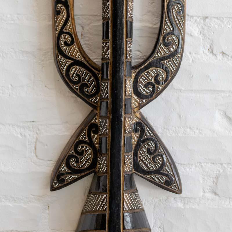 Detalhe dos grafismos de espirais e texturas pontilhadas em máscara decorativa artesanal de Bornéu.